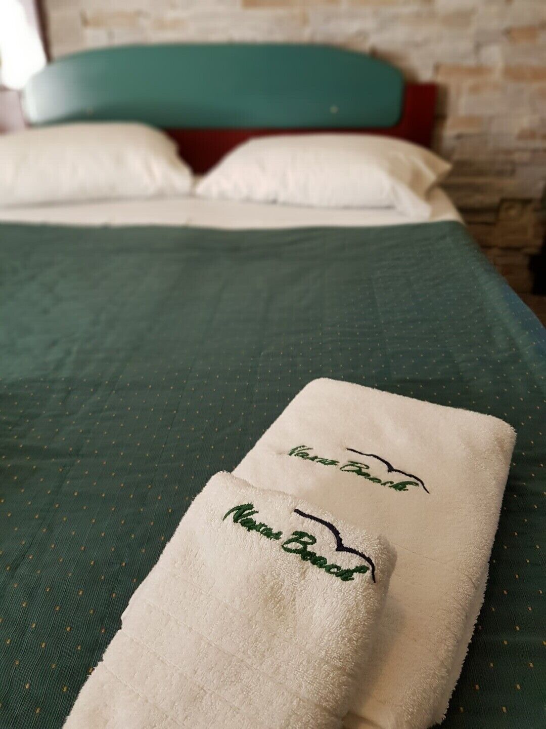 A neatly made bed with a green bedspread and two towels with embroidered text.