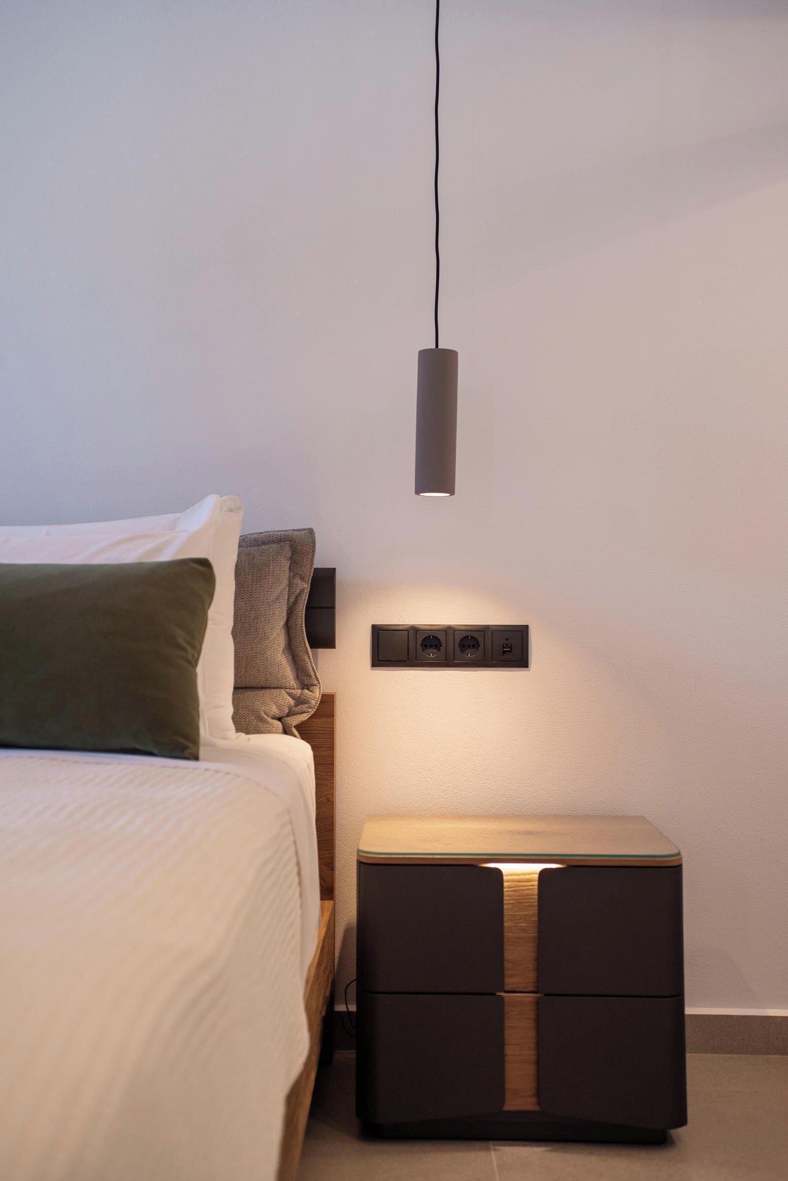 Ein modernes Schlafzimmer mit Bett, Nachttisch und einer Wandsteckdose.