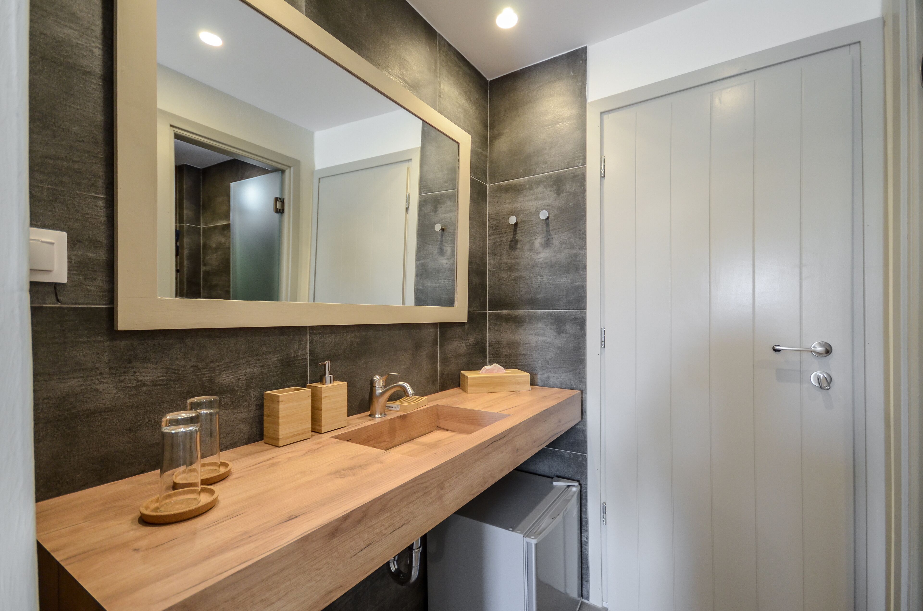 A modern bathroom with a wooden vanity, a large mirror, and a white door.