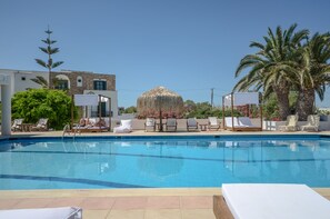 A swimming pool with lounge chairs and a thatched structure. - Naxos Beach Hotel (Naxos)