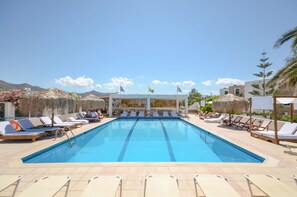 A swimming pool with lounge chairs and umbrellas, surrounded by buildings and flags. - Naxos Beach Hotel (Naxos)