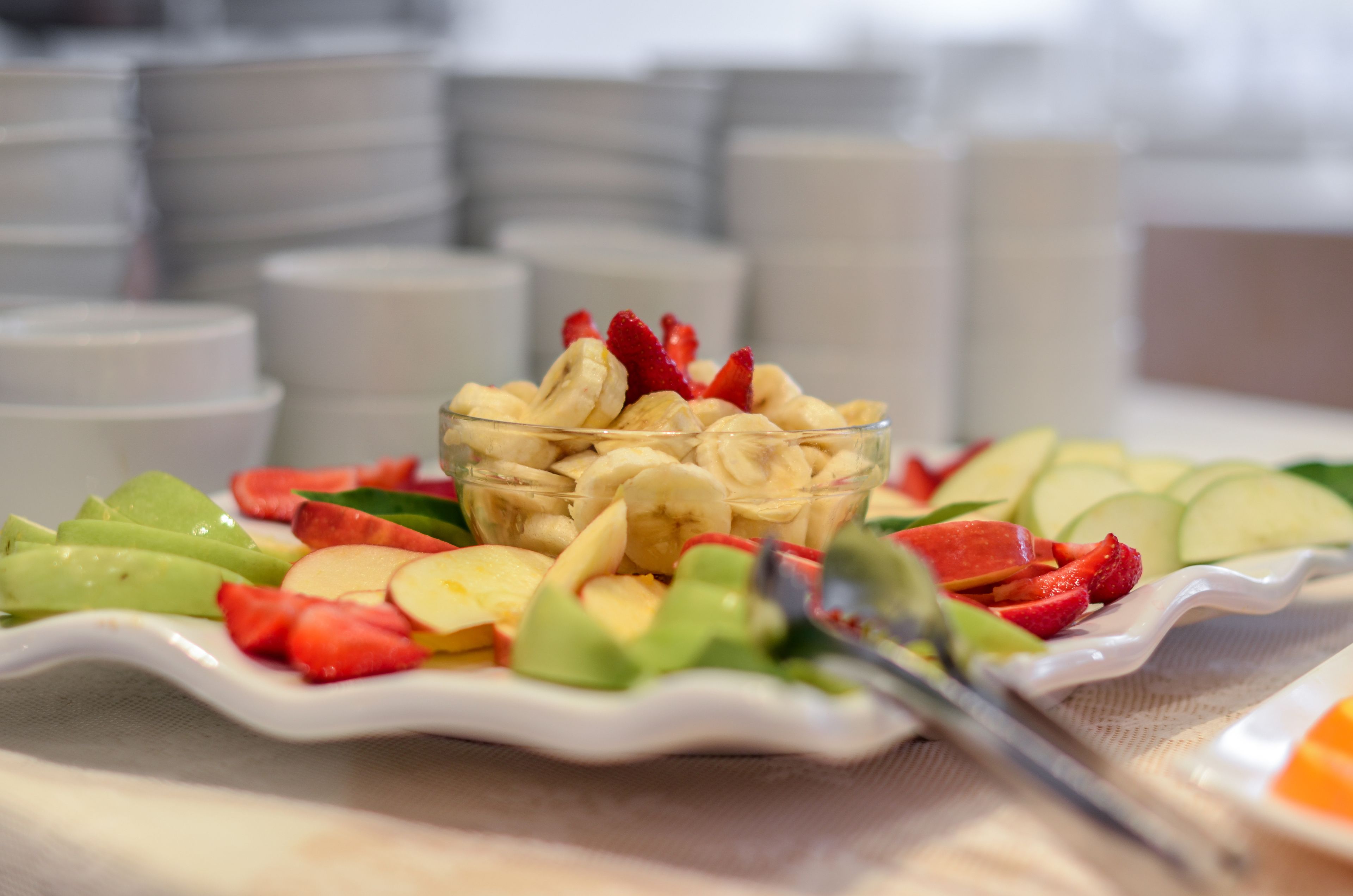 A breakfast buffet with a variety of fruits and a glass bowl of sliced bananas and strawberries.