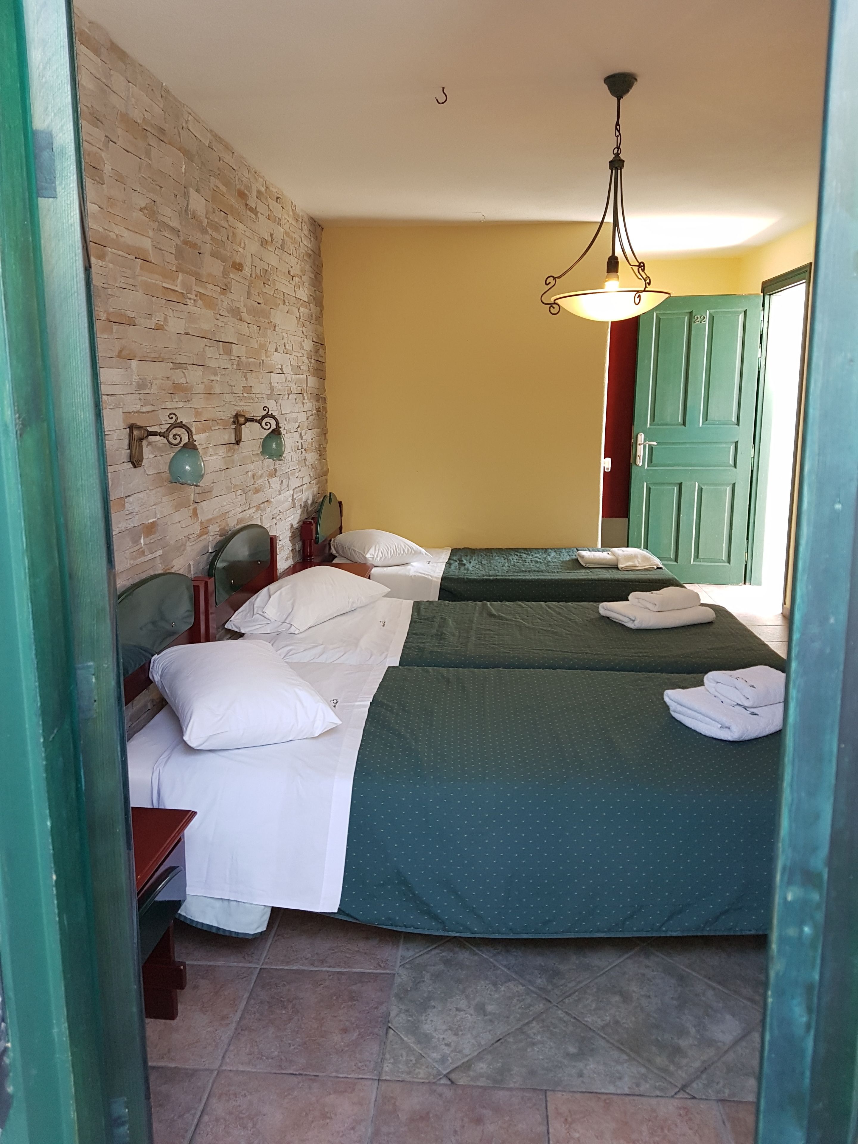 A room with two beds, a brick wall, a green door, and a hanging light fixture.