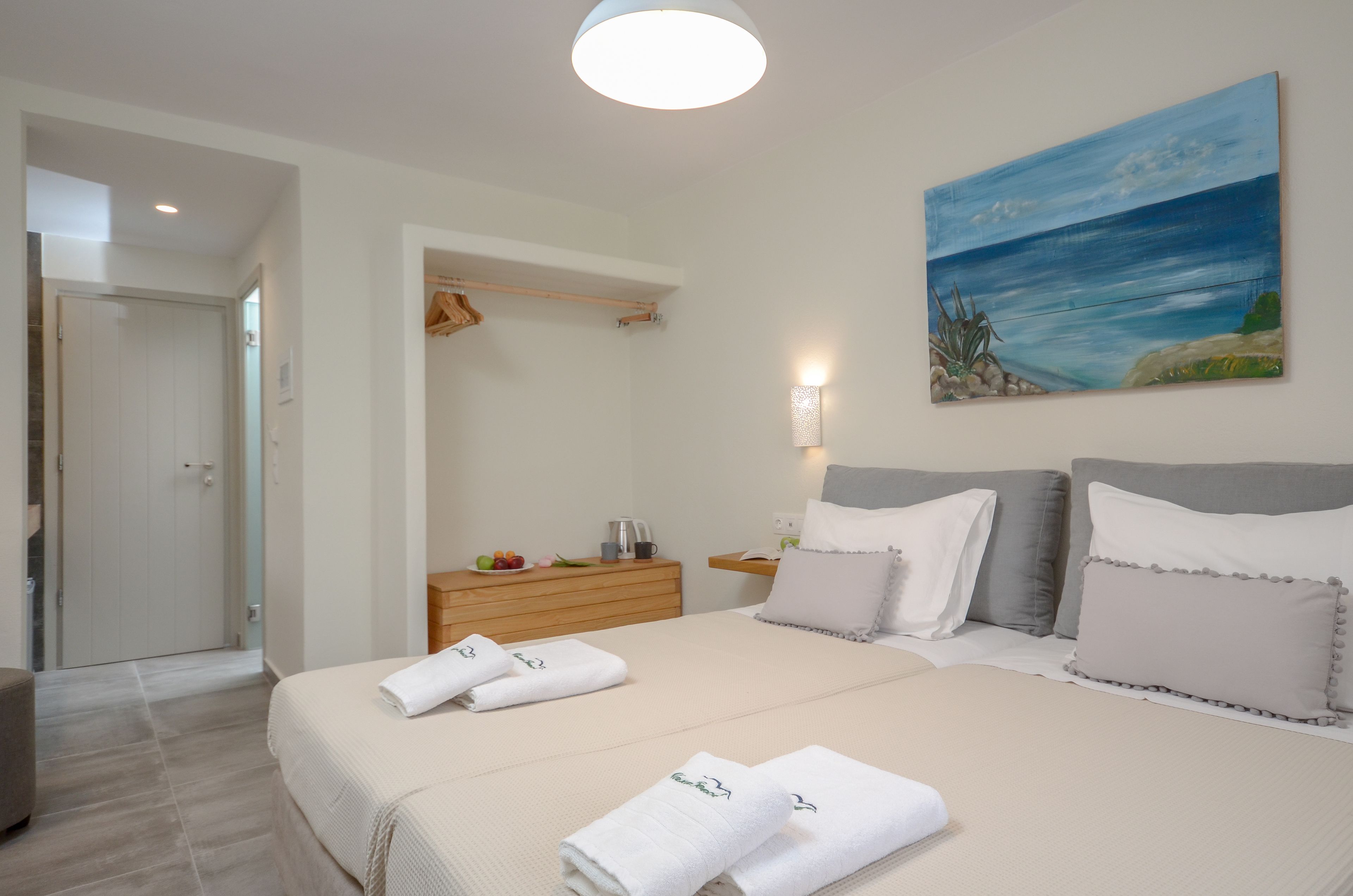Ein ordentlich eingerichtetes Hotelzimmer mit einem Bett, einem Nachttisch, einem Bild mit Strandmotiv und einem Kleiderschrank.