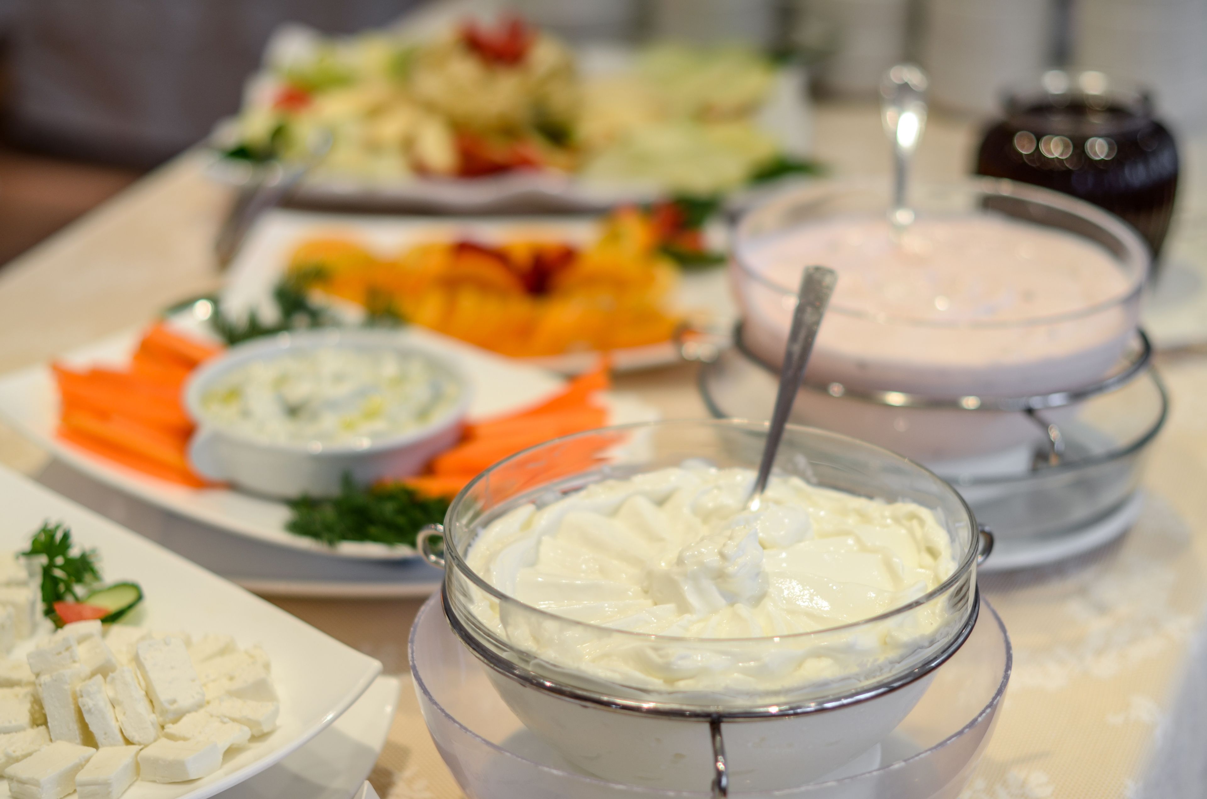 Une table de buffet proposant divers plats, notamment un saladier de cubes de fromage blanc, un bol de sauce crémeuse, ainsi que des assiettes de légumes et d’autres aliments.