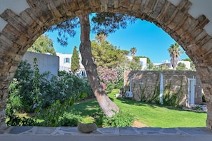 A stone archway framing a garden with a tree, a stone wall, and a building with a white door. - Naxos Beach Hotel (Naxos)