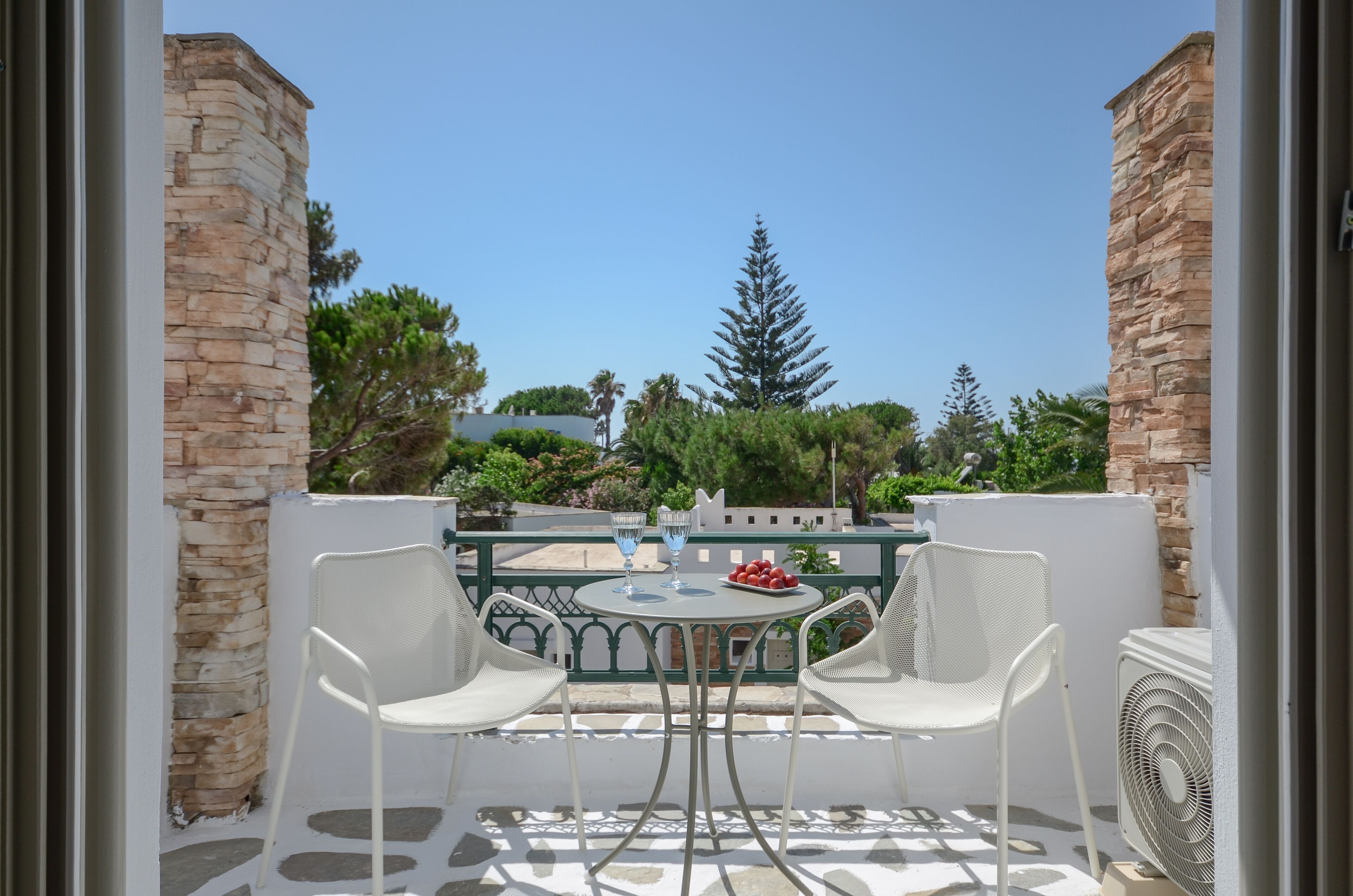 A balcony with a table and chairs, a fan, and a bowl of fruit.