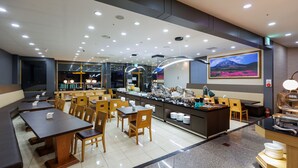 Un restaurant moderne doté de nombreuses tables et chaises, d’un buffet et d’un grand tableau accroché au mur.