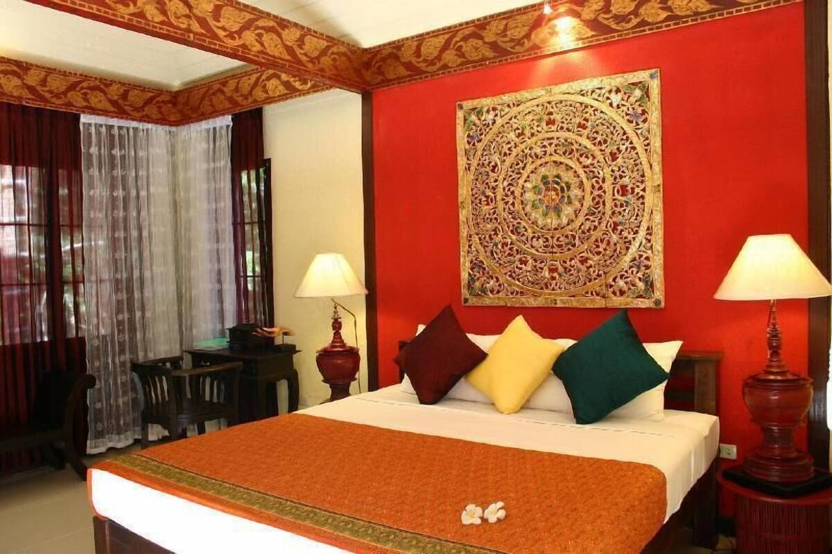 A hotel room with a bed, two bedside lamps, a decorative wall hanging, and a table with a lamp.