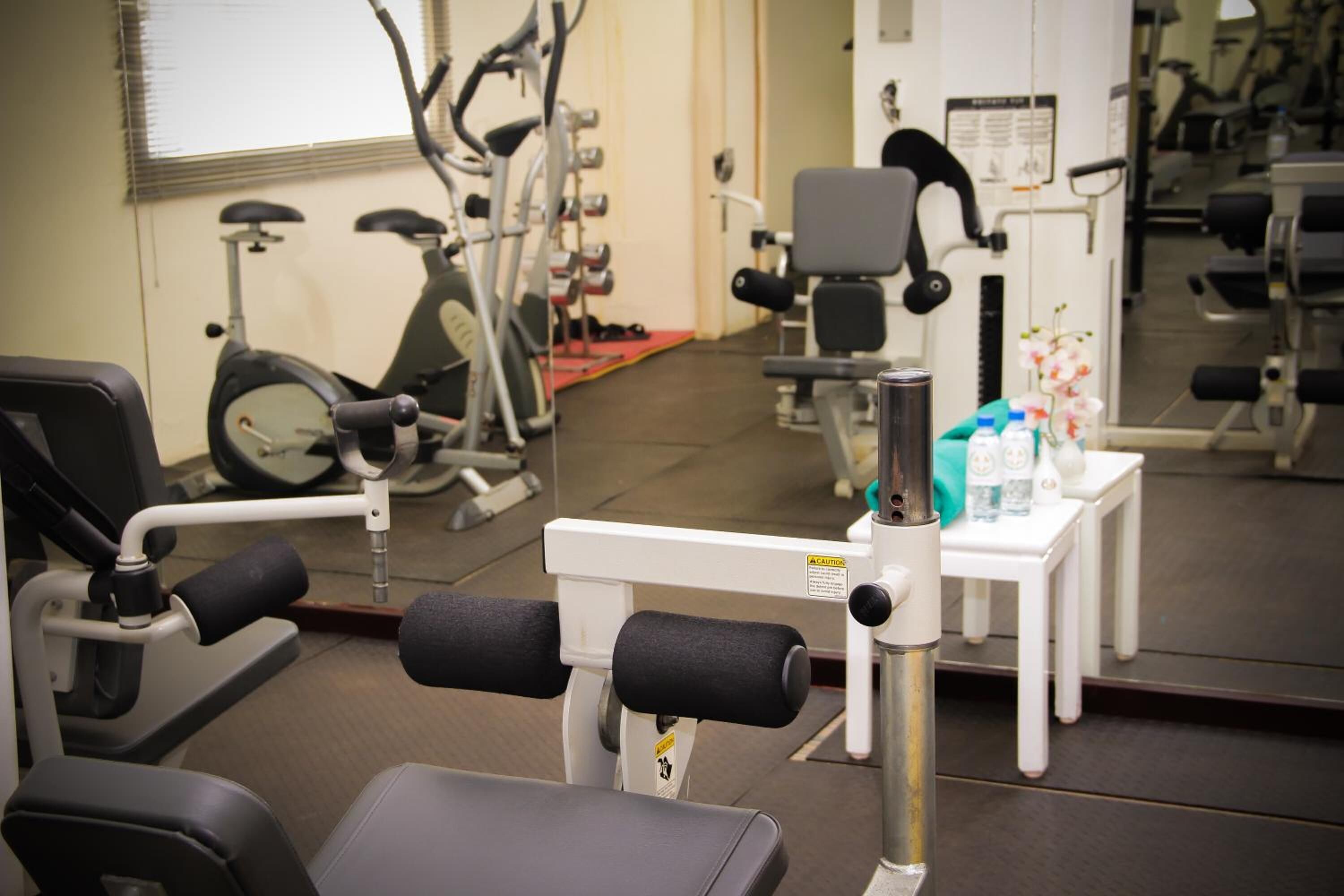 Une salle de sport équipée de matériel d’exercice, d’un miroir et d’une petite table sur laquelle sont posées des bouteilles.