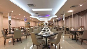 A spacious dining area with multiple tables and chairs, a central decorative light fixture, and a reflective ceiling. - Nova Park Hotel (Sharjah)