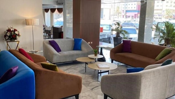 A modern lobby with a marble floor, a central seating area with sofas and armchairs, a coffee table, and a large window offering a view of the street. - Nova Park Hotel (Sharjah)
