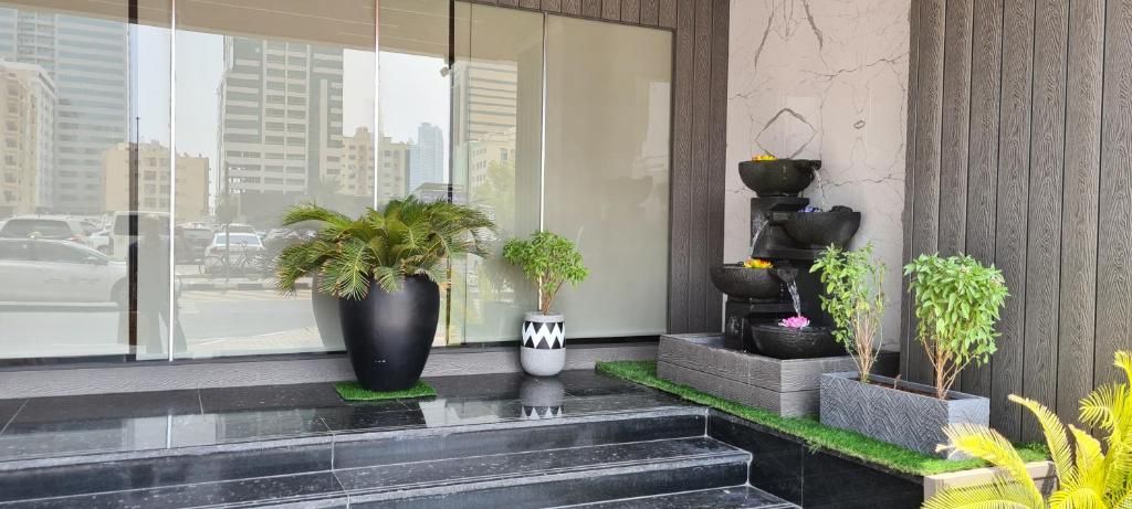 A modern building entrance with a glass door, a black marble staircase, and various potted plants.