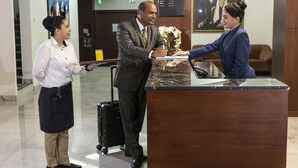 A reception area with a wooden reception desk, a digital display board, and a framed portrait on the wall. - Nova Park Hotel (Sharjah)