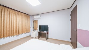 Hotellihuone, jossa on sänky, työpöytä, jossa on tietokone ja puhelin, televisio, ilmastointilaite ja ovi.