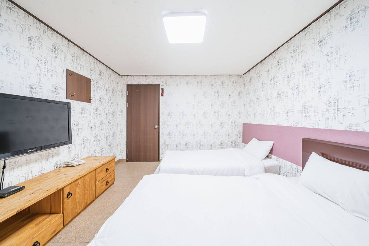 A hotel room with two beds, a TV, a wooden cabinet, and a door.