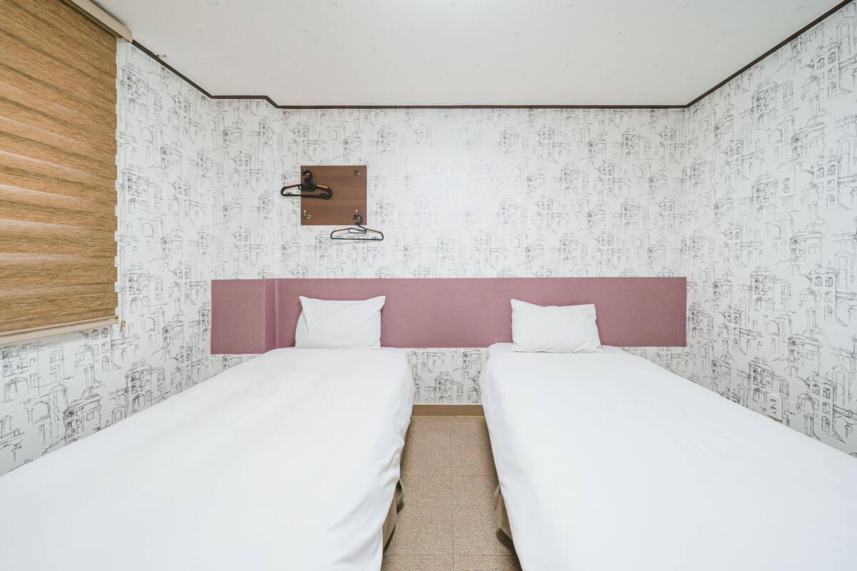 A room with two single beds, a wooden headboard, a wall-mounted hook, and patterned wallpaper.