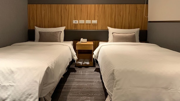 A hotel room with two beds, a wooden headboard, a nightstand with a phone, and a wall socket. - Yes Inn Taipei (Taipei)