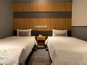 Two beds with white linens and pillows, a telephone, and a lamp on a nightstand.