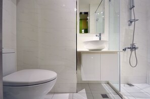 Features a sleek sink, glass-enclosed shower, and standard toilet in a clean-lined space.