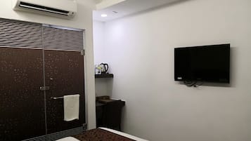 Habitación de hotel con ducha, cama, televisor montado en la pared y una pequeña mesa con tetera y tazas.
