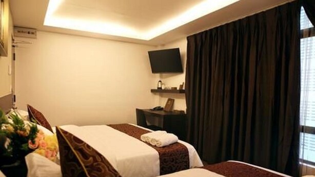 Habitación de hotel con dos camas, un televisor de pantalla plana, una mesita y un ventanal con cortinas.