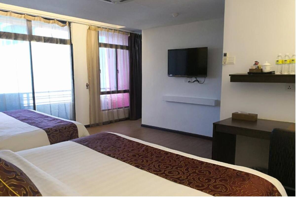 Een hotelkamer met twee bedden, een televisie, een bureau en een raam met gordijnen.