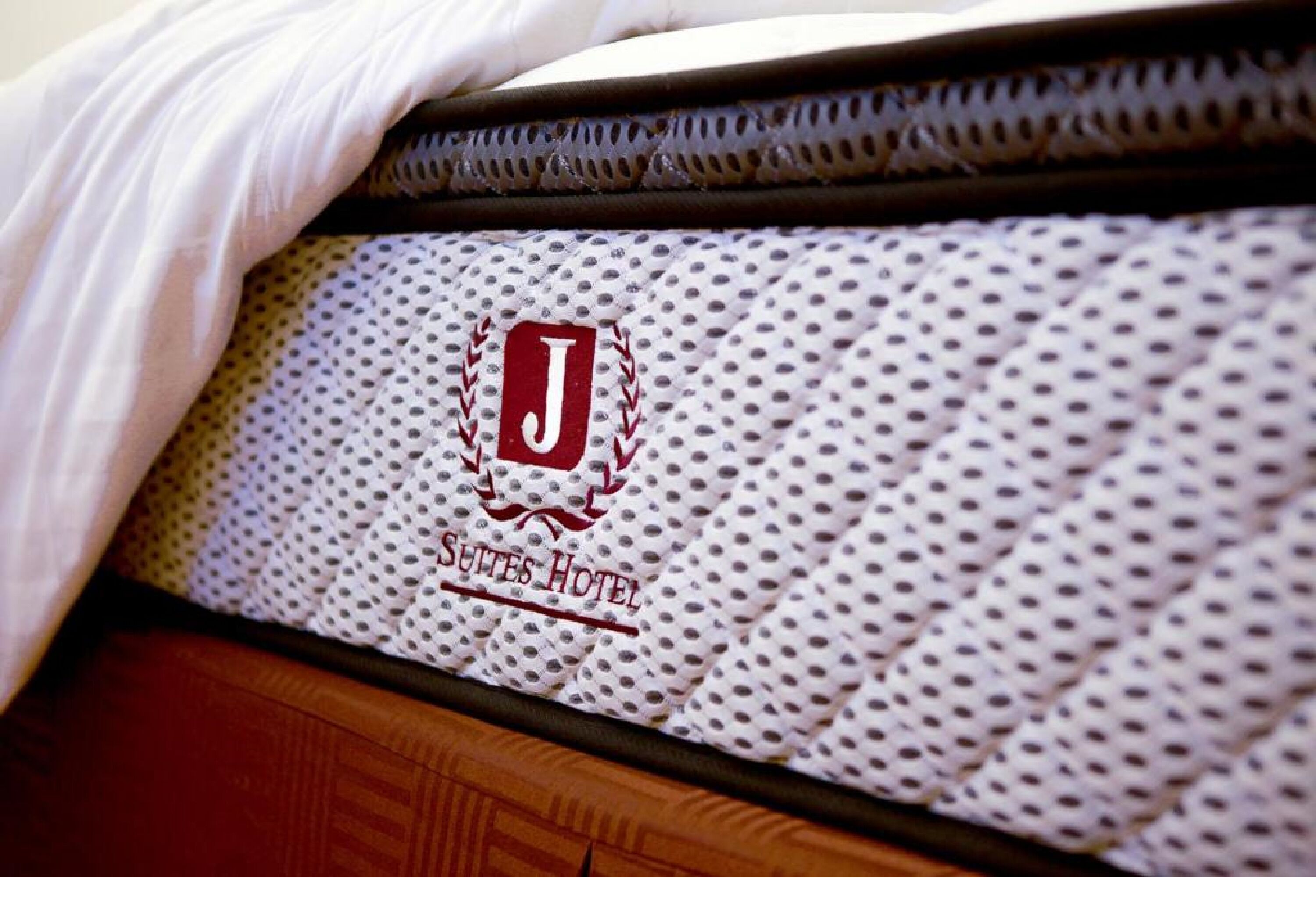 A bed with a quilted cover featuring a logo and text indicating it is part of the Suites Hotel.