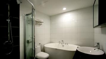 Et moderne badeværelse med en glasvæg omkring brusebadet, et hvidt toilet og et fristående badekar.