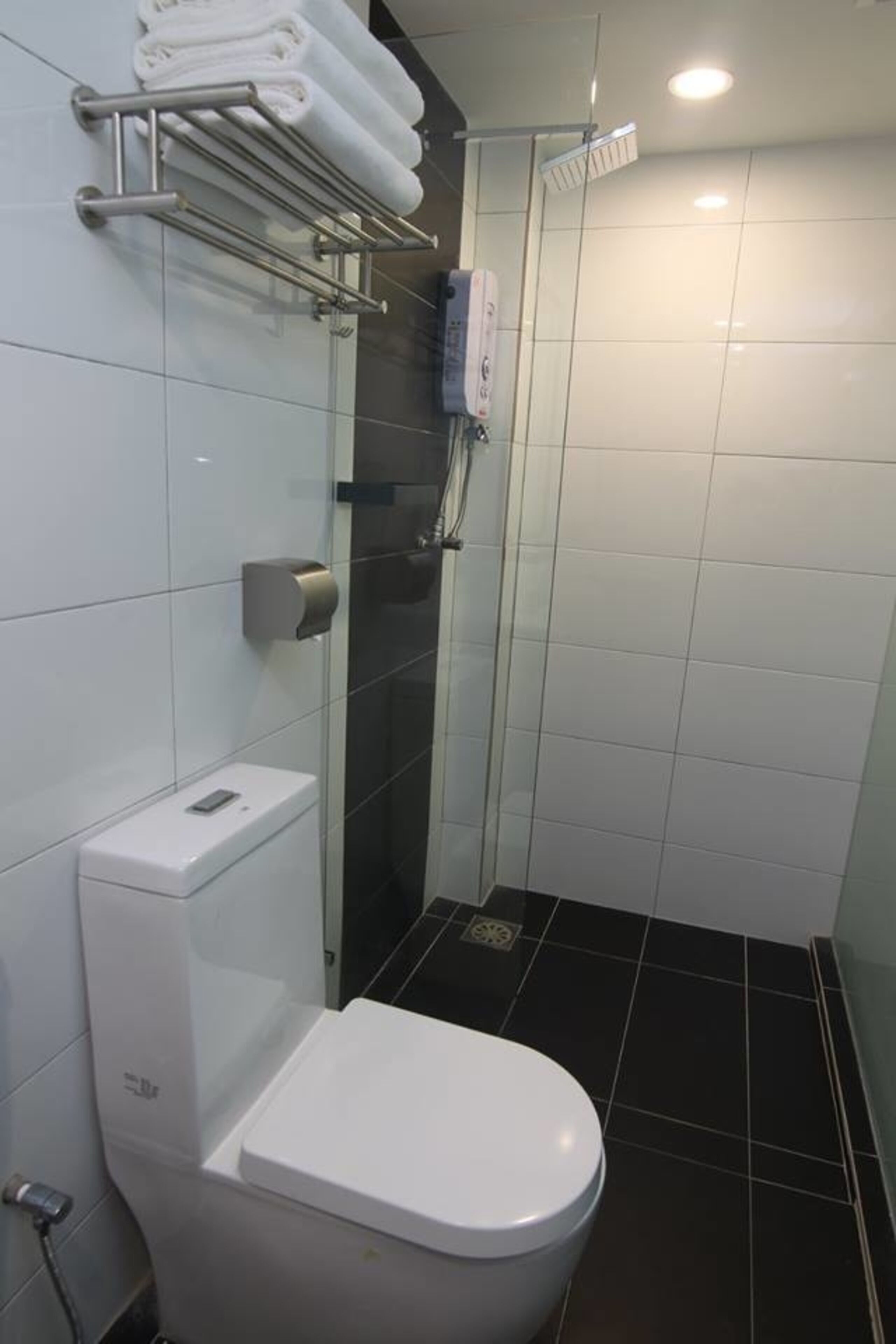 A modern bathroom with a white toilet, a glass shower enclosure, and a towel rack with folded towels.