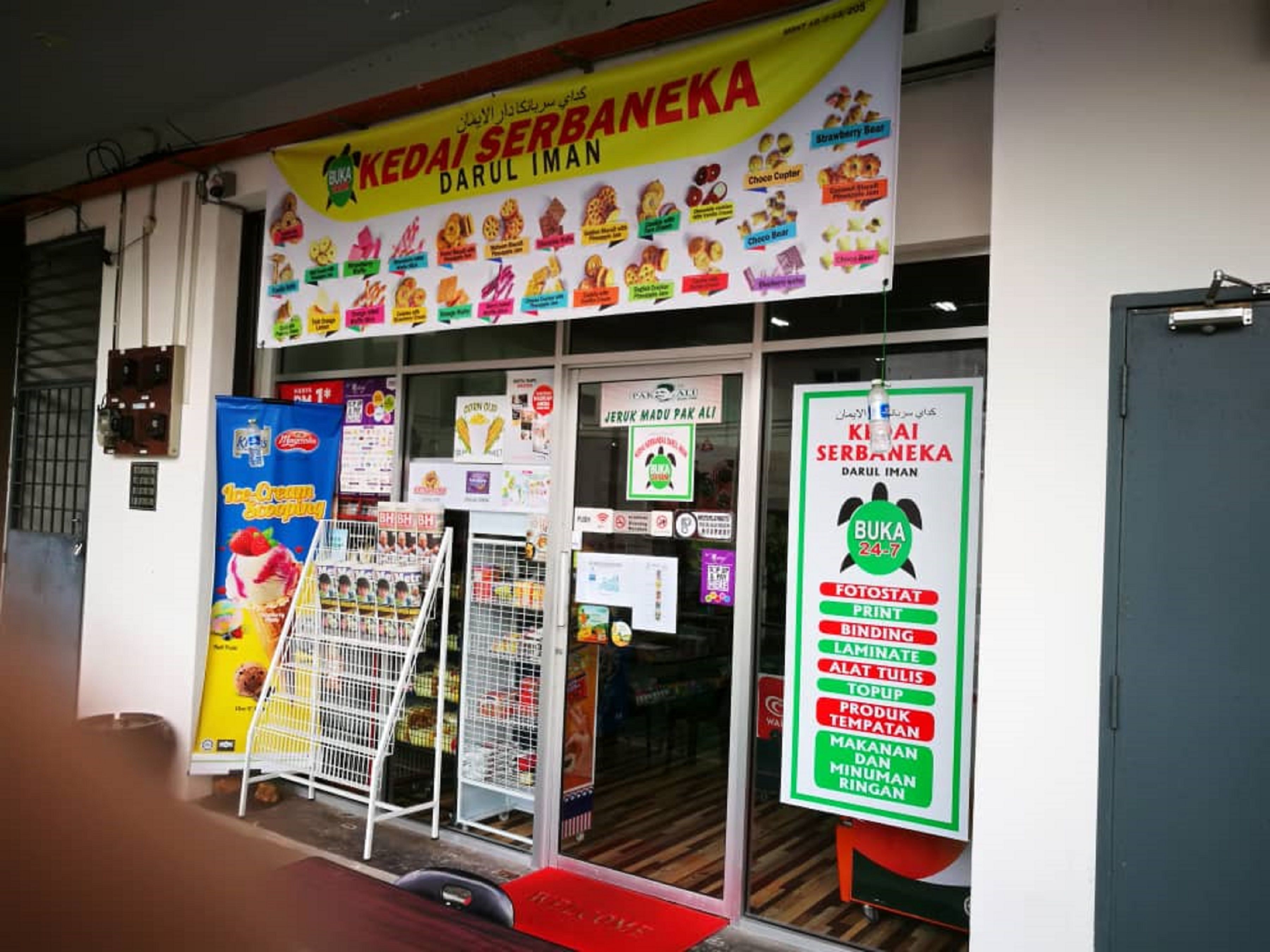 Un escaparate con un letrero que anuncia 'Kedai Serbaneka Darul Iman' y un menú de postres.