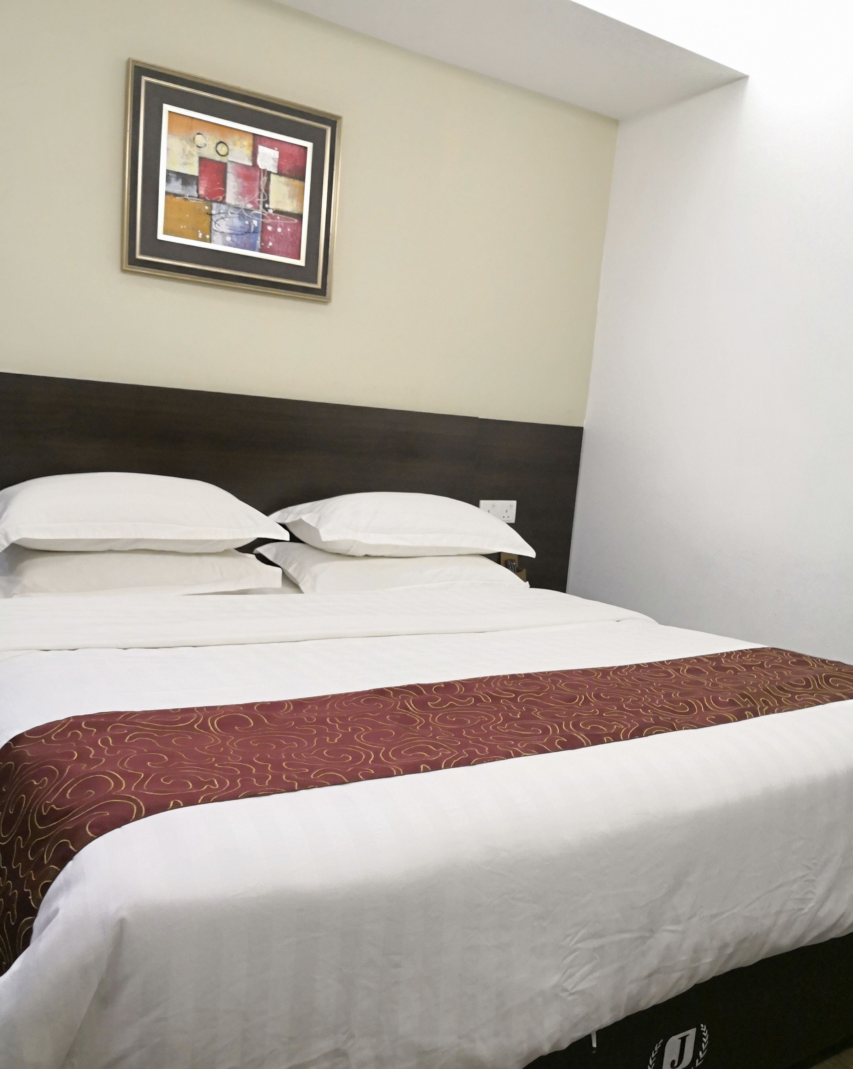 Quarto de hotel com cama, roupa de cama branca, cabeceira escura e uma obra de arte abstrata emoldurada na parede.