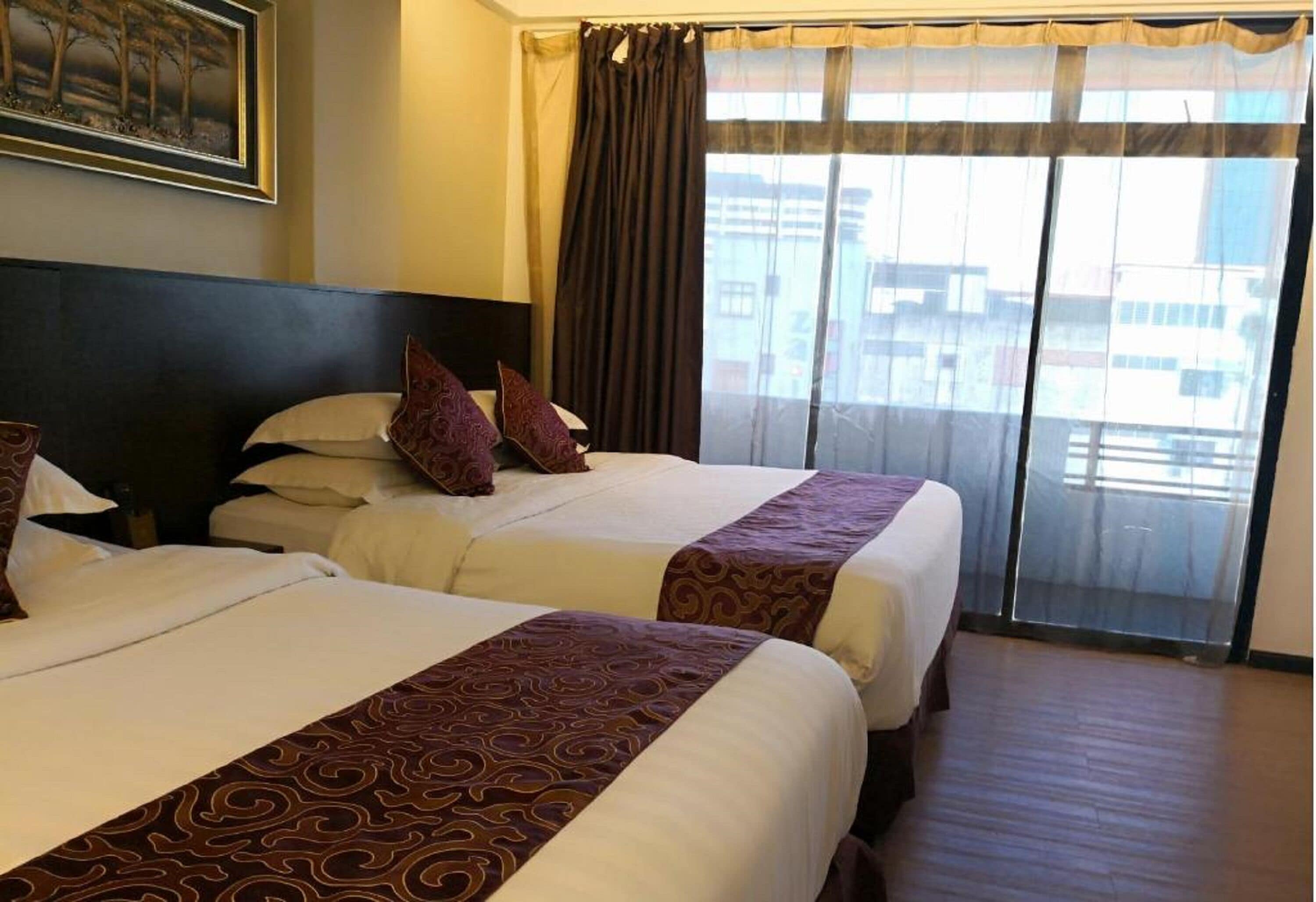 A hotel room with two beds, a large window with curtains, and a painting on the wall.