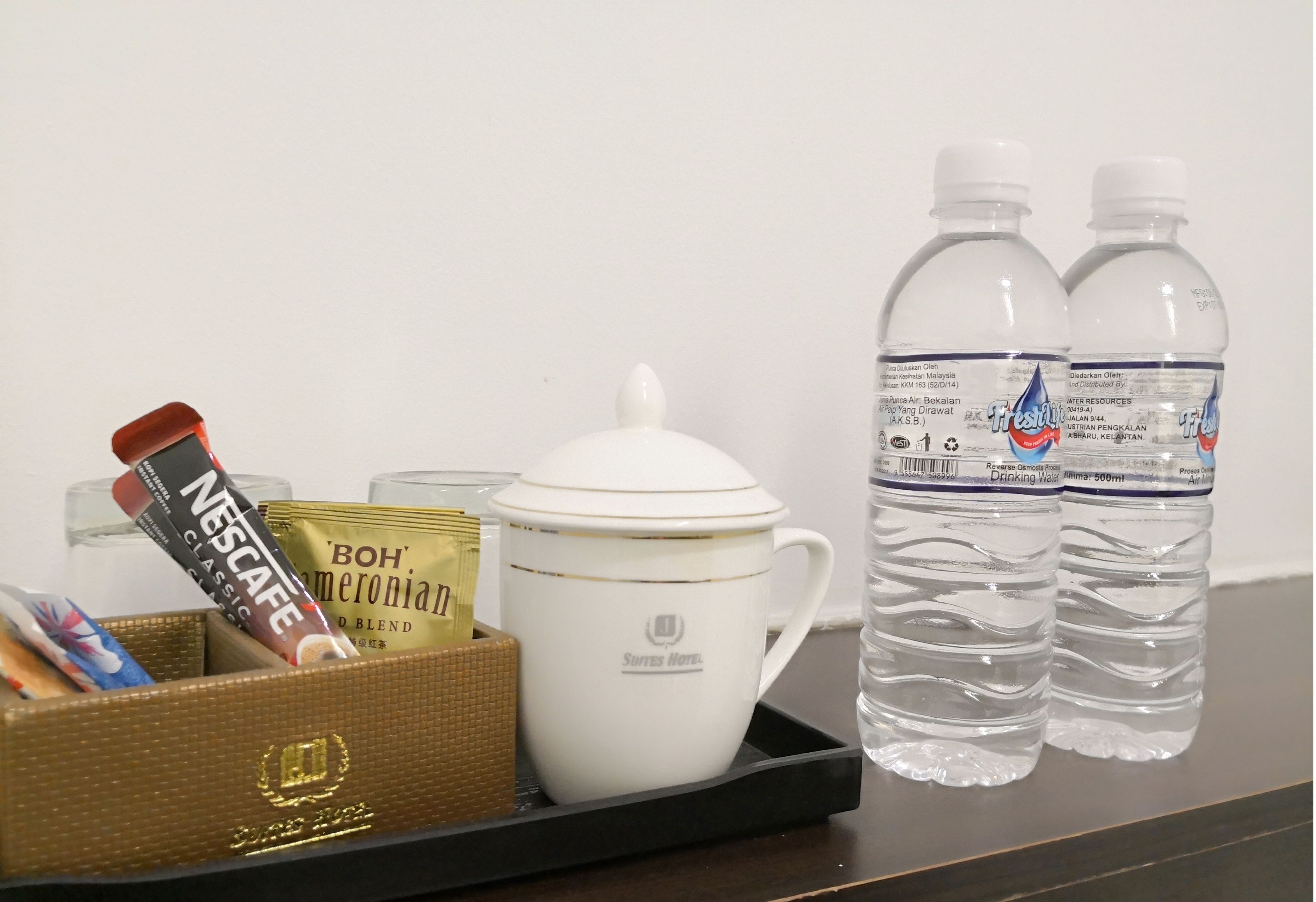 En bricka med en kaffemugg, ett paket Nescafe Classic-kaffe, ett paket Bohn's Americano-kaffeblandning och två vattenflaskor.