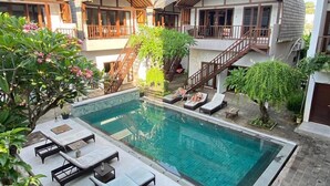A pool area with lounge chairs and a staircase leading to a building with multiple balconies. - Naturela Uluwatu (Pecatu)