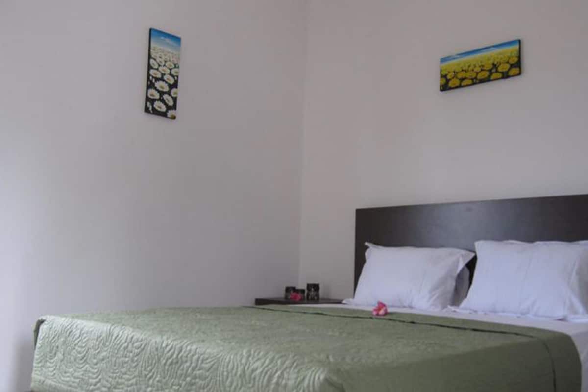 Uma cama de solteiro com roupa de cama branca e um edredom verde num quarto com paredes brancas.