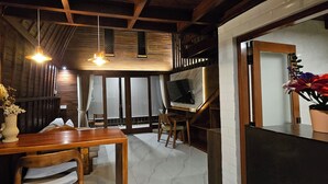A cozy room with wooden walls, a wooden dining table, and a TV on a stand. - Naturela Uluwatu (Pecatu)