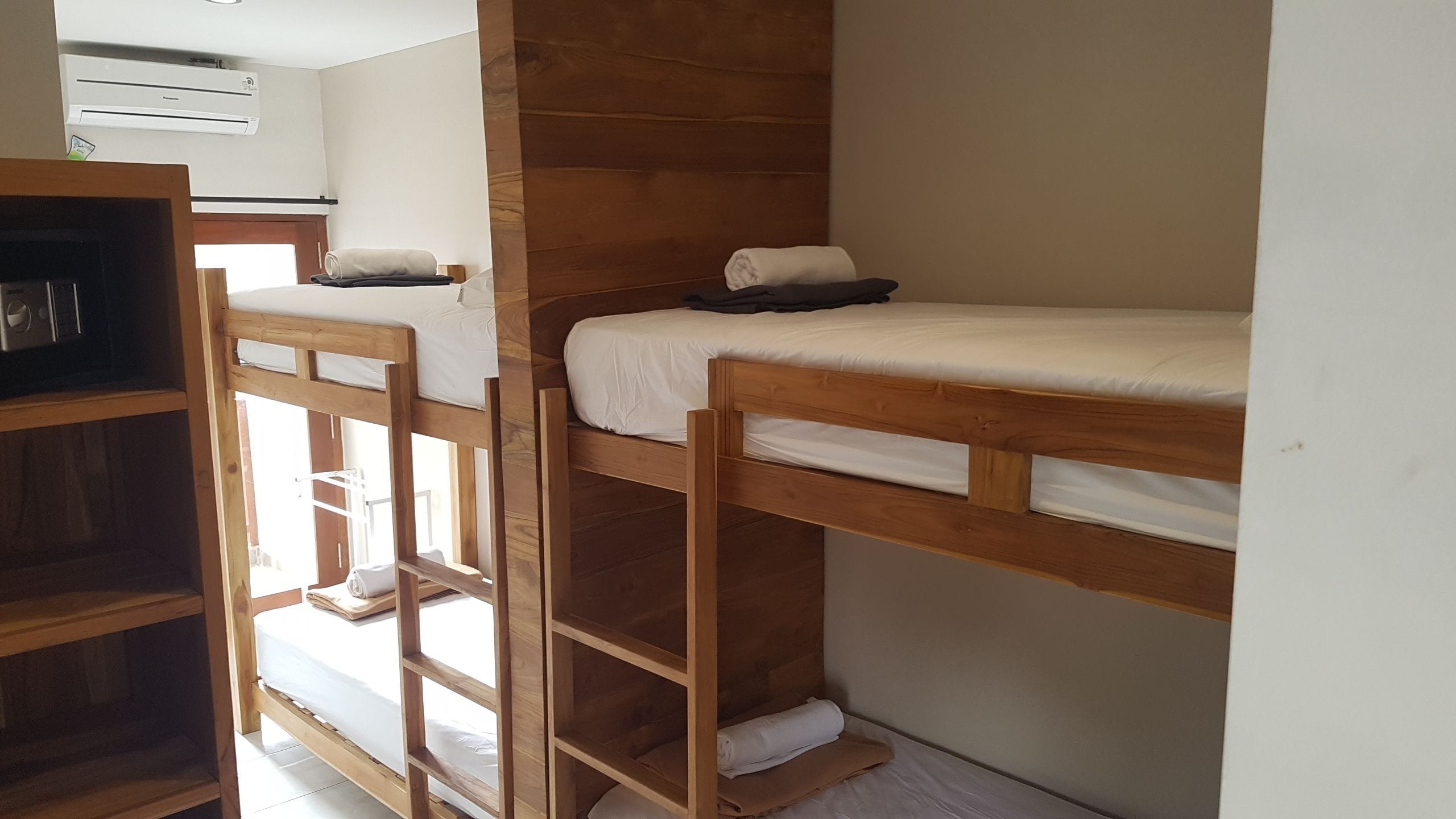 Habitación con literas de madera, un colchón blanco y una pequeña estantería.
