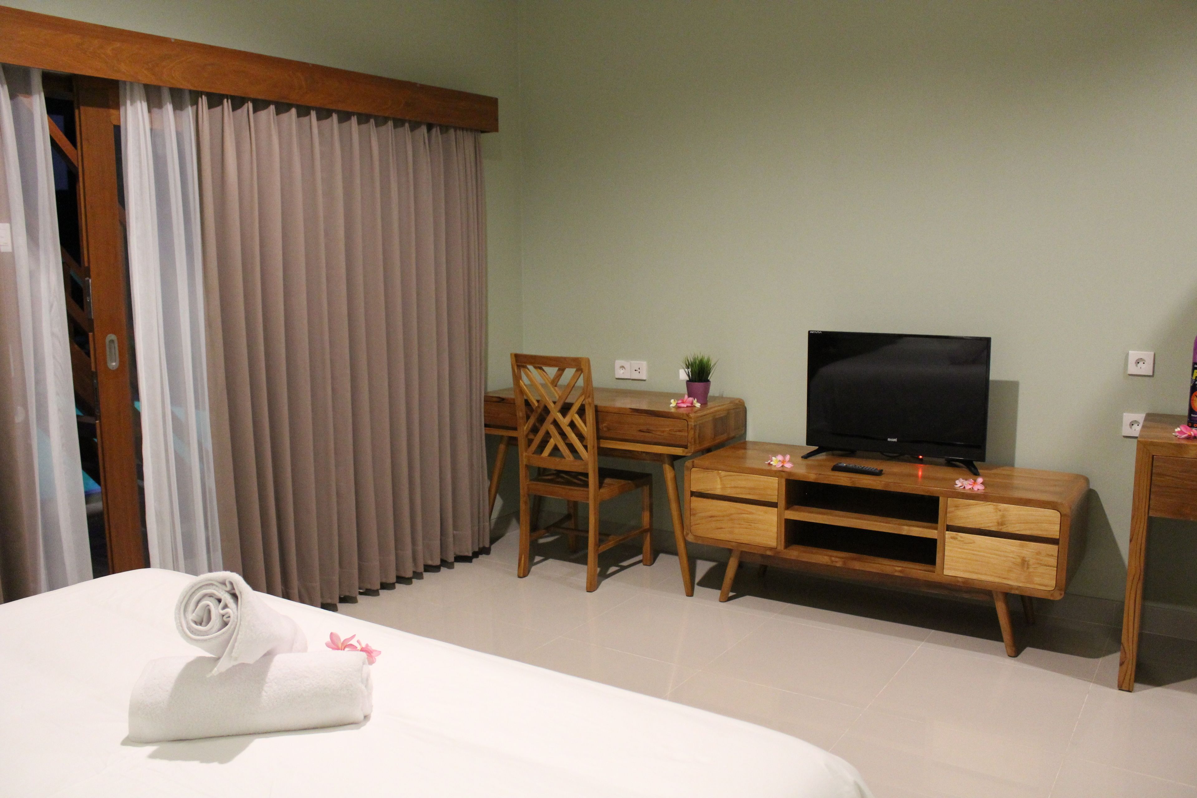 Une chambre d’hôtel avec un lit, un bureau en bois avec une télévision, une chaise et une plante en pot.