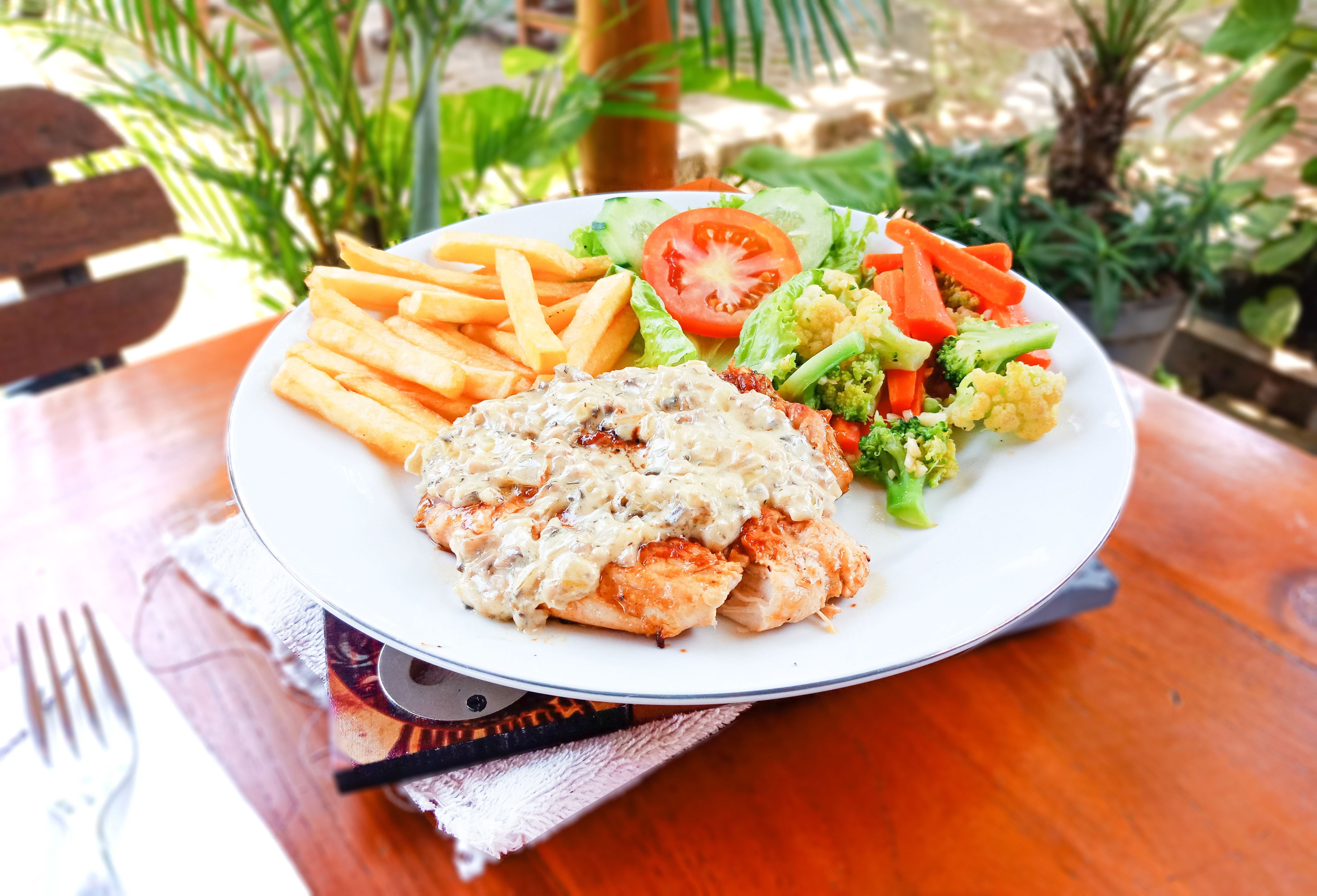 A plate of food including a salad, fries, and a chicken dish on a wooden table.