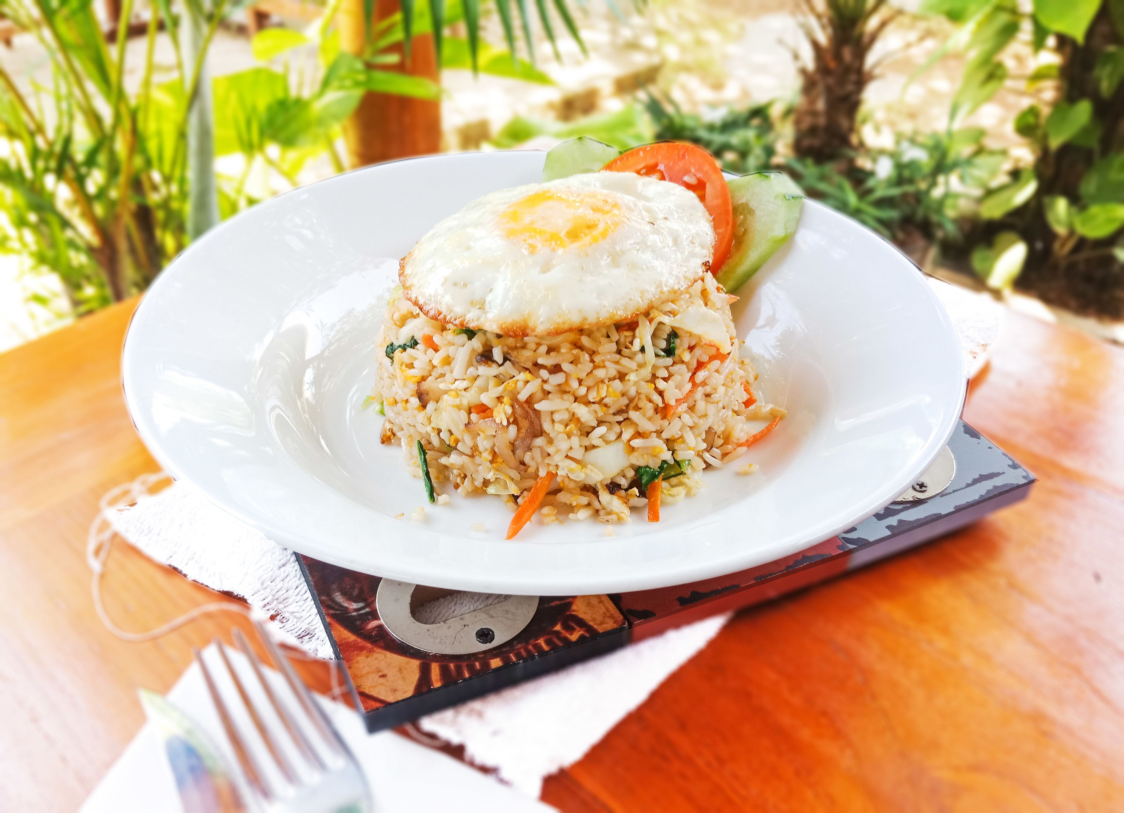 A plate of fried rice with vegetables and a fried egg on a white plate.