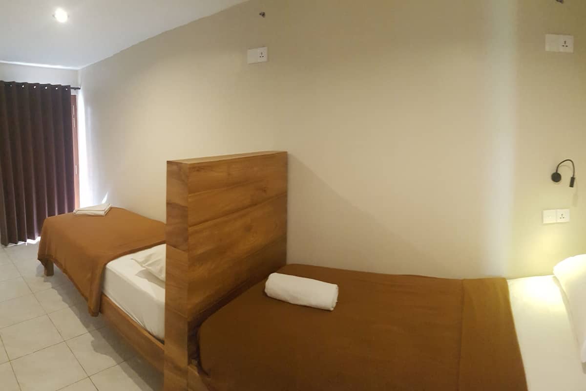 Quarto de hotel com duas camas de solteiro, cabeceira de madeira, mesa de cabeceira e telefone fixado na parede.