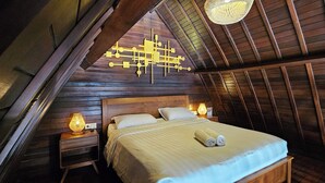 A cozy attic bedroom with a wooden sloped ceiling, a bed with white linens, and two bedside lamps. - Naturela Uluwatu (Pecatu)