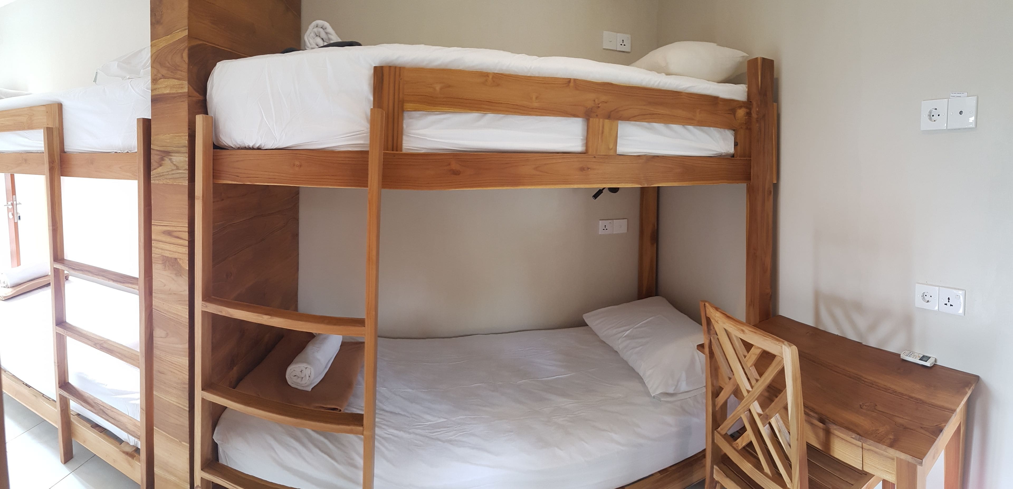 Een stapelbed met bureau en stoel, een stopcontact en een raam.