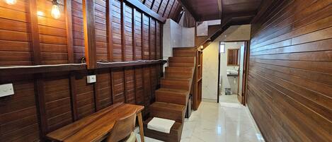 A hallway with wooden paneling, a marble floor, and a wooden staircase leading to a bathroom.