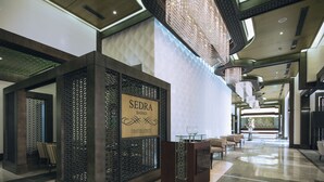 Un vestíbulo moderno con un mostrador de recepción, un cartel que indica el restaurante 'SEDRA BAWADI' y un área de descanso con sillas.