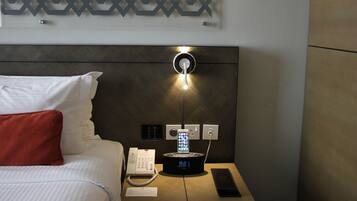 A hotel room with a bed, a bedside table with a phone and a charging station, and a wall-mounted light fixture.