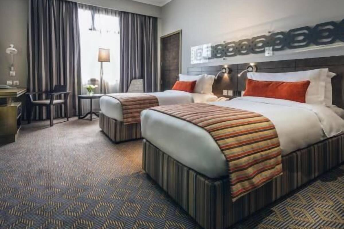 A hotel room with two beds, a desk, a chair, and a large window with curtains.