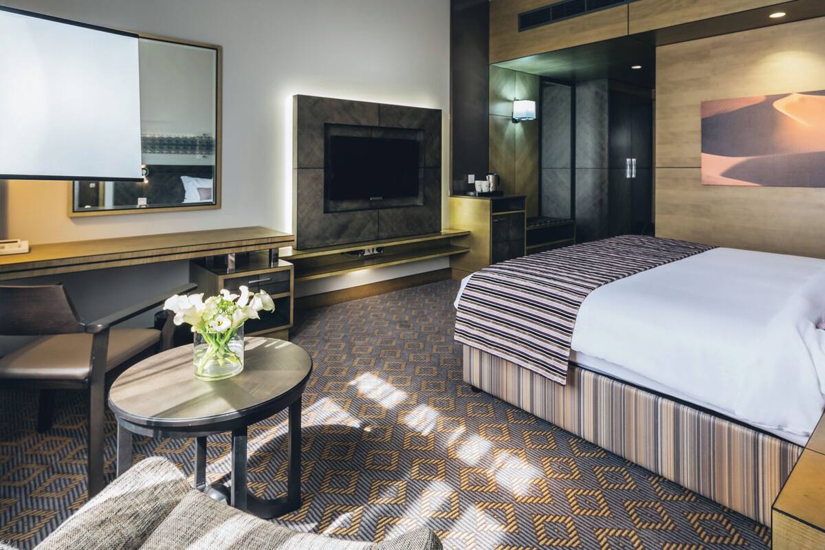 A hotel room with a bed, a TV, a desk, and a chair.