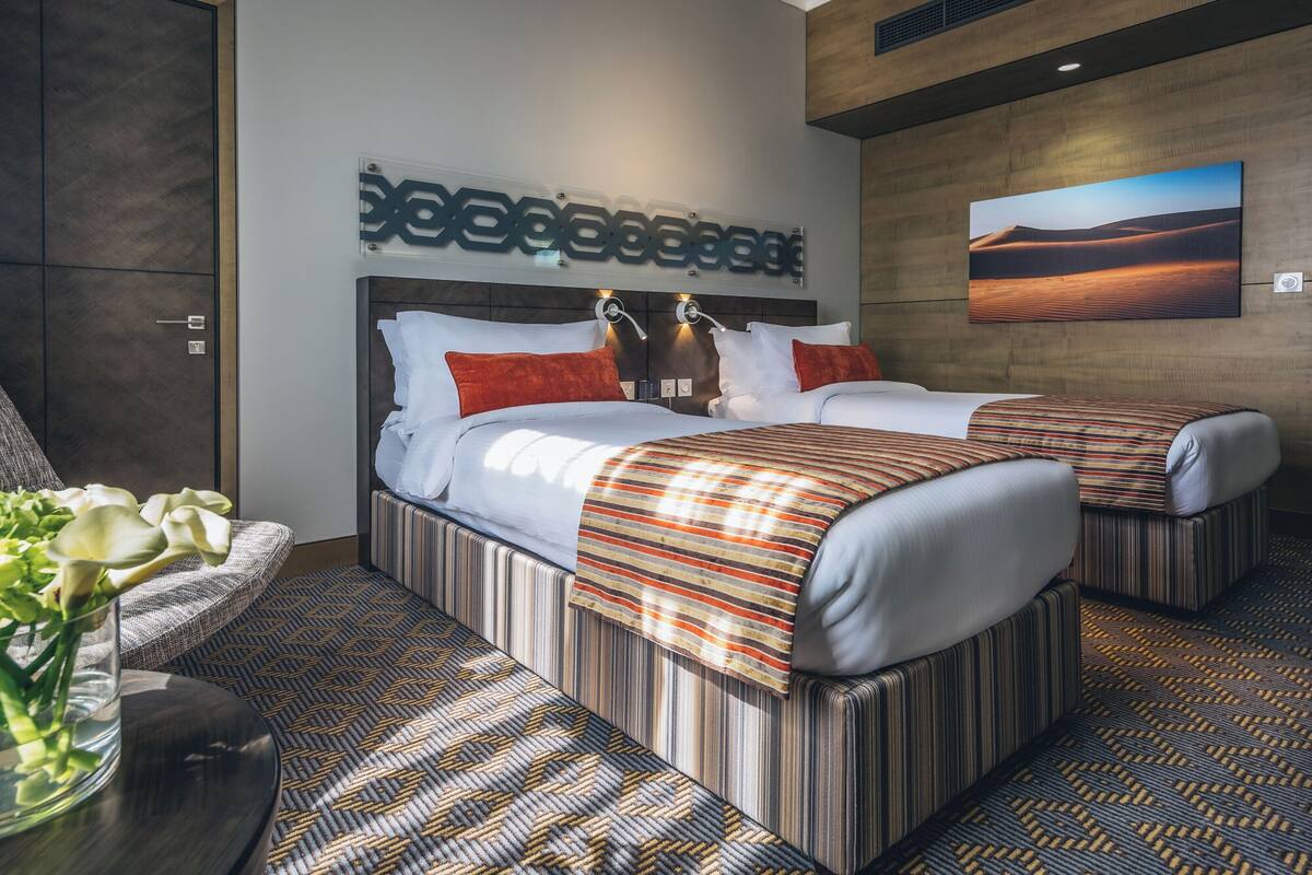 A modern hotel room with two beds, a large wall art piece, and a view of a desert landscape.